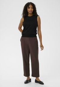 Zwarte mouwloze top gecombineerd met losse bruine broeken en zwarte schoeisel. De outfit heeft een minimalistisch ontwerp met een soepele textuur.