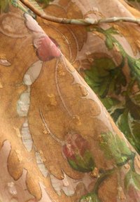 Tissu léger brun clair avec motifs floraux verts et roses et petits points texturés dispersés sur la surface.