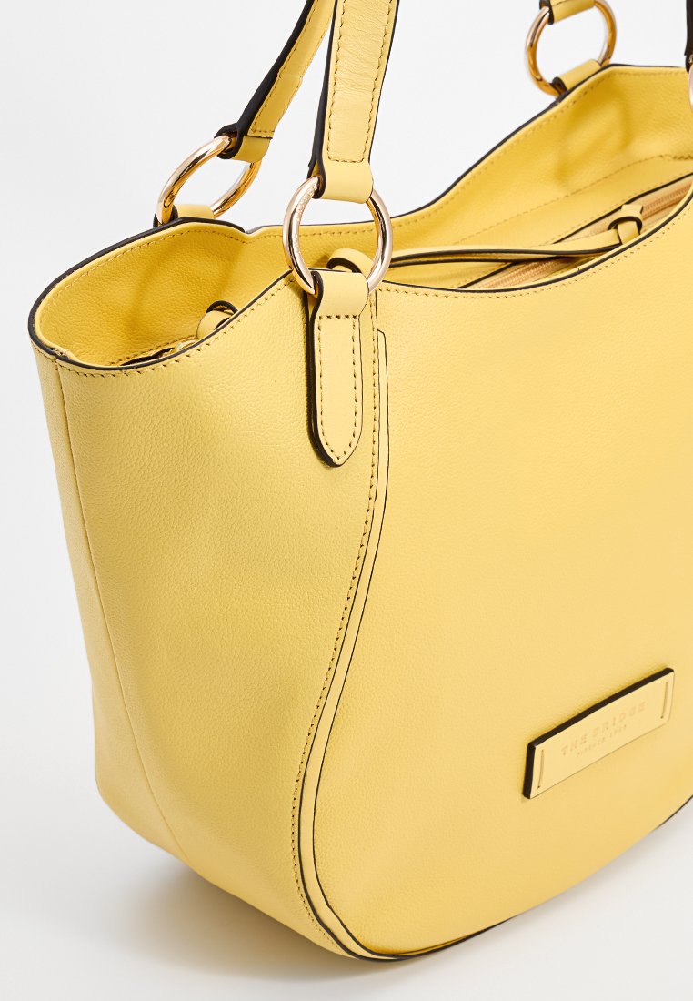 Borsa a mano gialla in pelle con dettagli neri, texture liscia, design arrotondato, doppio manico con accessori dorati e etichetta del marchio in rilievo.