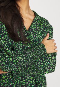 Green and black patterned shirt featuring a smocked cuff, button-down front, and a soft fabric with a floral design.