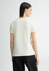 Cremefarvet T-shirt med korte ærmer lavet af blød bomuld, med rund halsudskæring og en afslappet pasform, parret med mørke jeans.