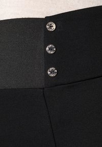 Pantalones negros con una tela suave, cinturilla ancha y tres botones metálicos en la parte superior de la cintura para el cierre.
