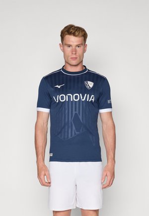 Maillot de football bleu marine à manches courtes avec des accents blancs, comportant des rayures verticales et un logo sur la poitrine. Fabriqué en matériau léger.