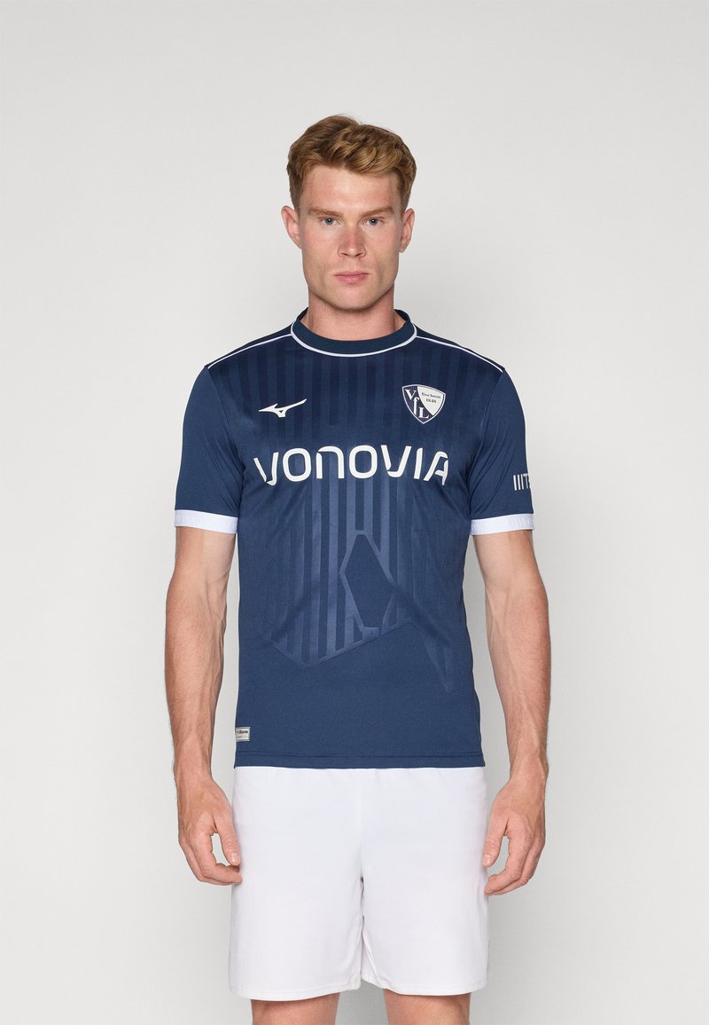 Camiseta de fútbol de manga corta azul marino con acentos blancos, que presenta rayas verticales y un logo en el pecho. Fabricada con material ligero.