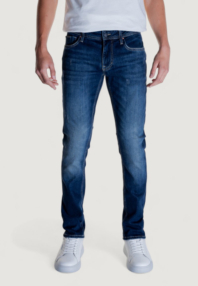 Jeans de mezclilla azul con un corte ajustado, que presentan un lavado desgastado, sutiles marcas de roce y un diseño clásico de cinco bolsillos. Combinados con zapatillas blancas.