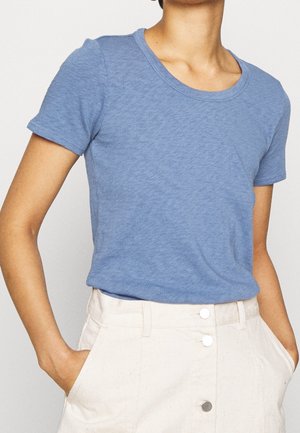 Person wearing a light blue short-sleeve crew neck t-shirt tucked into high-waisted beige pants with front buttons and pockets.