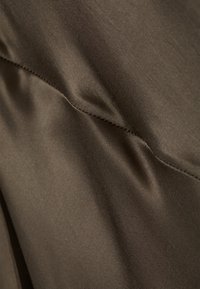Brown fabric with a smooth texture and slight sheen. Features a seam with subtle folds and soft draping, indicating flexible material.