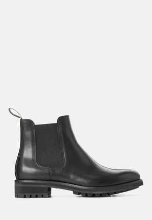 Black leather Chelsea boot with elastic side panels, rubber sole, and a pull tab. Smooth finish, rounded toe, and lug tread for traction.