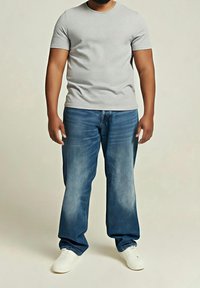 T-shirt gris manches courtes associé à un jean bleu délavé, offrant une coupe décontractée. Des baskets blanches complètent la tenue casual.