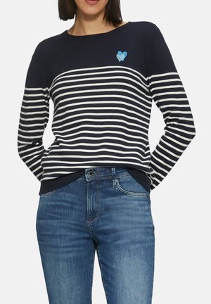 Pull rayé bleu marine et blanc avec un col rond, arborant un emblème de cœur bleu. Complété par un jean en denim bleu.
