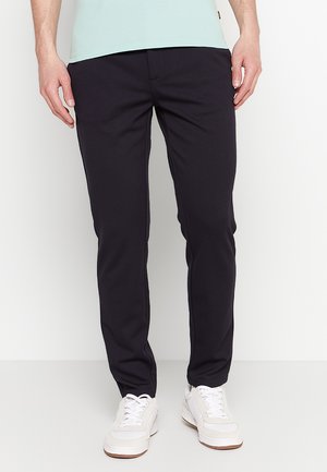 Dunkelmarinefarbene, schmal geschnittene Hose aus elastischem Material mit glatter Textur und minimalistischem Design. Kombiniert mit weißen Sneakers.