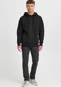 Sudadera negra con cordón, de corte relajado. Combinada con pantalones oscuros ajustados y zapatillas deportivas de color claro.
