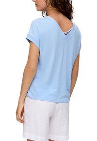 Lichtblauw T-shirt met korte mouwen, een V-hals en gekruiste banden op de rug, gemaakt van een zachte katoenmix, gecombineerd met witte shorts.