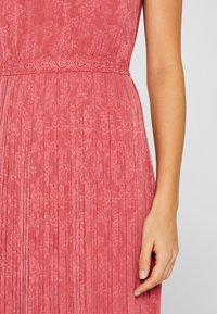 Plisované midi šaty z látky v růžové barvě, s květinovým vzorem a zdobeným krajkovým páskem. Hladká textura s elegantním splýváním.