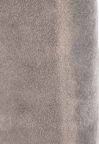 Gros plan d'un tissu en daim beige doux montrant une surface fine et texturée avec des fibres légèrement surélevées et des variations subtiles de nuances.