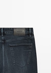 Jeans in denim scuro con una texture liscia, design dritto, cinque tasche, e un'etichetta in pelle con la scritta "Massimo Dutti" stampata sulla cintura.
