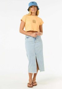 Top corto naranja claro con un gráfico, combinado con una falda de mezclilla azul claro que presenta una abertura frontal y un dobladillo deshilachado. Sombrero de cubo azul y sandalias.