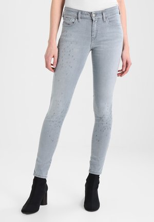 Jeans ajustados en denim gris claro con detalles desgastados, diseño de cinco bolsillos y cintura a media altura, combinados con botas negras hasta el tobillo.