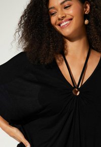 T-shirt noir à manches larges, avec un décolleté en V profond et un détail en forme de découpe circulaire. Fabriqué en tissu doux avec une coupe décontractée.