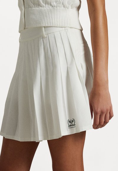 Valkoinen laskostettu hame korkealla vyötäröllä, jossa on pieni Wimbledon-logo helman lähellä ja sileä pinta.
