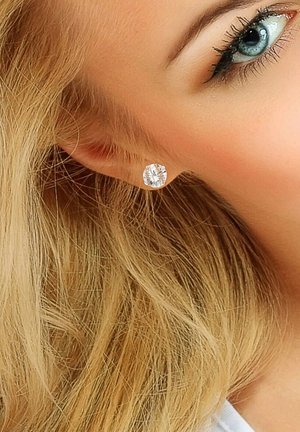 Boucles d'oreilles en cristal rond serties dans un simple cadre en argent, présentées de manière proéminente contre des cheveux blonds clairs. Surface brillante et réfléchissante.