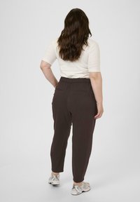 Brune joggerbukser med elastisk talje og sidelommer, parret med en lysefarvet tætsiddende top og grå sneakers.