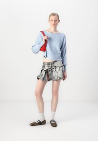 Lys blå cropped genser, grå denimskjørt med belte og folder, og brune sko med leopardmønster. Modellen holder en rød håndveske.
