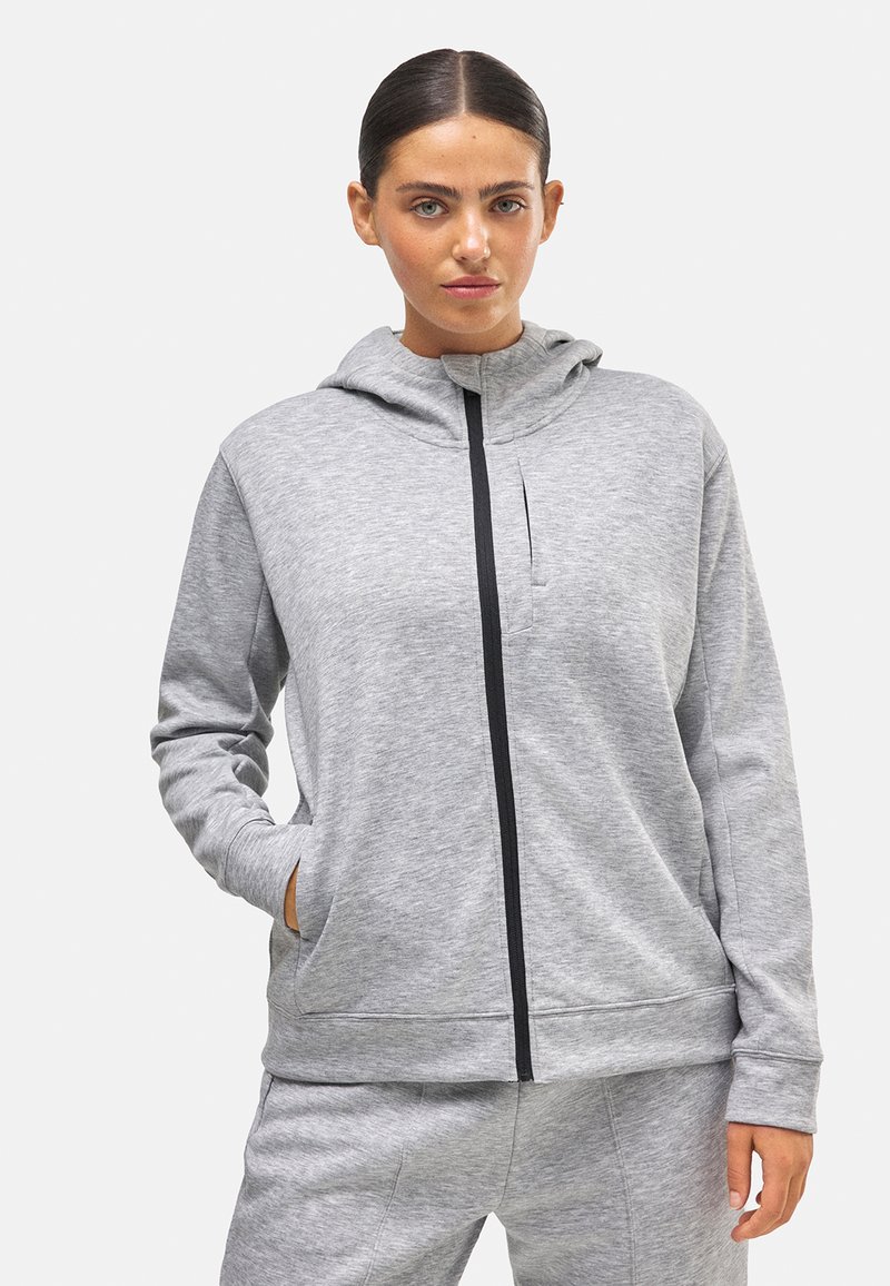 Sudadera gris con cremallera, hecha de material suave, que cuenta con un bolsillo frontal, un cuello alto y detalles en cremallera negra. Textura suave en toda la prenda.