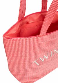 Borsa tote intrecciata rosa con esterno testurizzato, doppi manici e chiusura con zip. L'interno è foderato in tessuto liscio con una tasca.
