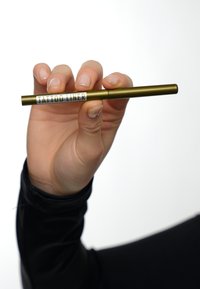 Penna eyeliner per tatuaggi tenuta in mano; corpo metallico dorato con testo bianco; forma cilindrica; superficie liscia; punta affilata per un'applicazione di precisione.
