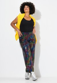Bodysuit negro con cárdigan de punto amarillo, combinado con pantalones cubiertos de purpurina multicolor. Botines plateados con cordones. Textura suave.
