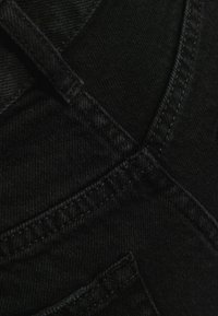 Black denim fabric with a smooth texture, featuring visible stitching and a small pocket detail, emphasizing its sturdy design and color.