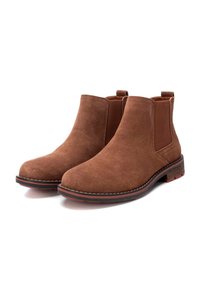 Botas Chelsea de ante marrón con punta redondeada, paneles laterales elásticos y una suela texturizada con un ligero acento rojo alrededor de la base.