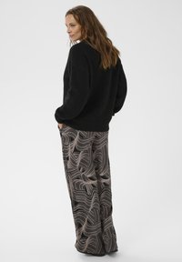 Un pull en tricot noir à coupe décontractée, associé à un pantalon large avec un motif de lignes tourbillonnantes en beige et noir.
