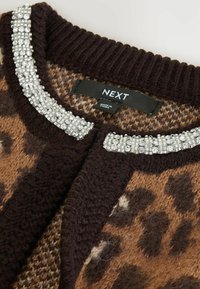 Cardigan z leopardskim vzorcem v rjavi in črni barvi, ki ima širok okrašen ovratnik s prozornimi bleščicami. Oznaka pravi "NEXT."