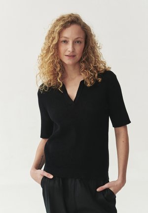 Maglione nero lavorato a maglia a maniche corte con scollatura a V. Texture liscia e vestibilità rilassata, abbinato a pantaloni neri larghi.