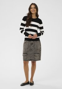 Pull rayé noir et blanc à col rond, associé à une jupe en denim gris avec poches avant et ourlet effiloché, porté avec des ballerines noires.