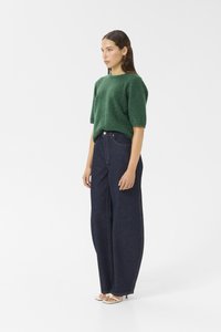 Green knitted sweater with a relaxed fit, paired with high-waisted dark blue wide-leg jeans. The outfit features subtle stitching details.