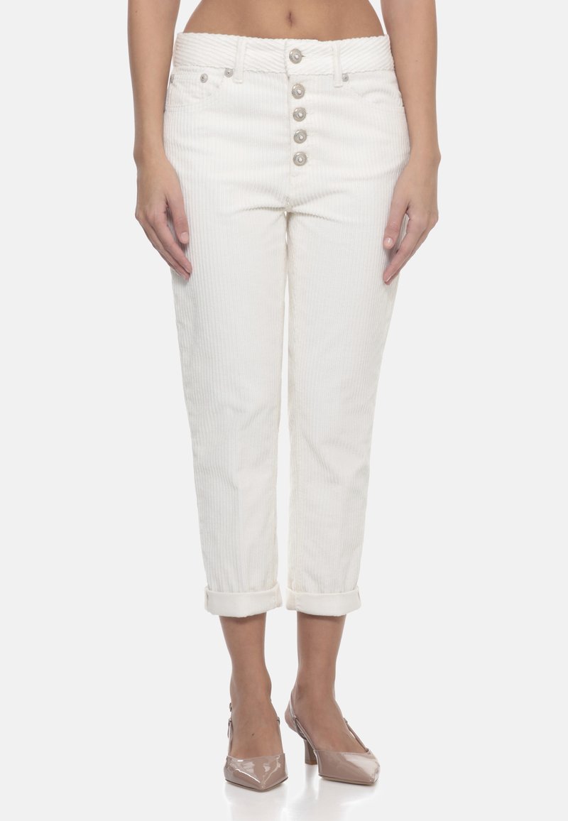Donna che indossa pantaloni cropped in corduroy bianco a vita alta con cinque bottoni e risvolti, abbinati a tacchi in pelle lucida color nude.