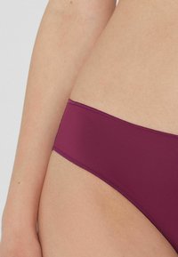Bordeauxfarbene Bikini-Hose aus glattem Stoff, mit einem niedrigen Schnitt und minimalen Nähten entlang der Kanten für einen nahtlosen Look.