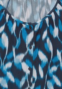 Blusa con motivo blu e bianco, realizzata in un tessuto testurizzato, con scollo rotondo e sei bottoni scuri lungo la parte anteriore.
