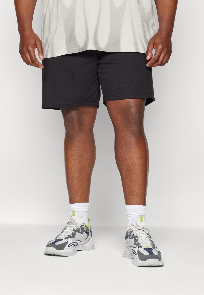 Shorts noirs en matériau doux, associés à des baskets grises et blanches texturées avec des accents néon, portées avec des chaussettes blanches.