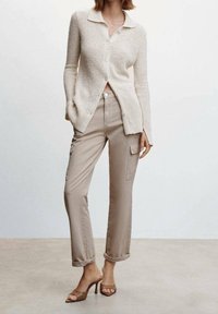 Cardigan beige tricoté avec un col, associé à un pantalon cargo beige clair avec poches latérales et bords retroussés, porté avec des sandales à talons brunes.