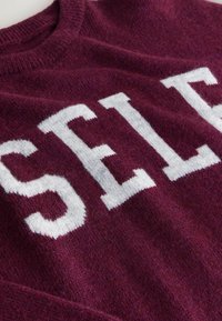 Burgundy knit sweater with large white "SELF" text, featuring a round neckline and soft, textured fabric.