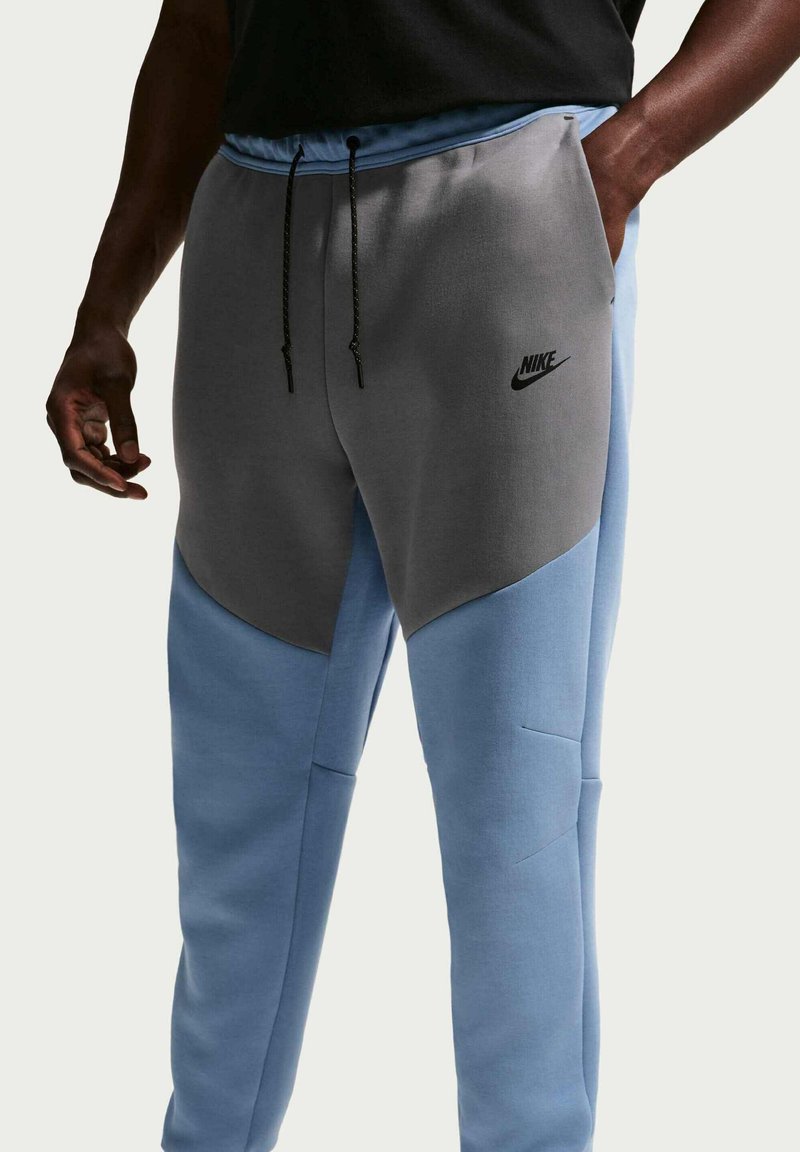 Pantaloni jogger Nike con schema di colori grigio e azzurro chiaro, tessuto morbido, design aderente e coulisse nera con dettaglio logo sulla coscia.