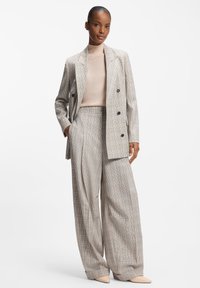 Beżowa, dwurzędowa marynarka w kratę zestawiona z wysokim stanem szerokich spodni. Gładka tkanina z subtelnym wzorem w kratę oraz neutralny golf.