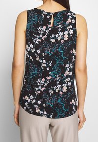 Top negro sin mangas con un estampado floral en rosa y verde azulado, que presenta un detalle de ojal en la parte posterior y una tela suave y ligera.