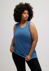 Blauw mouwloos top met een V-hals ontwerp, gemaakt van een zachte stof. Heeft een losse pasvorm en valt onder de heupen, gecombineerd met zwarte broeken.