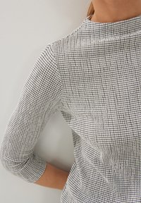 Gestreifte Weste in Schwarz-Weiß-Karo; verfügt über einen hohen Kragen und drei Viertelärmel. Glatte Textur mit leichtem Stretch.