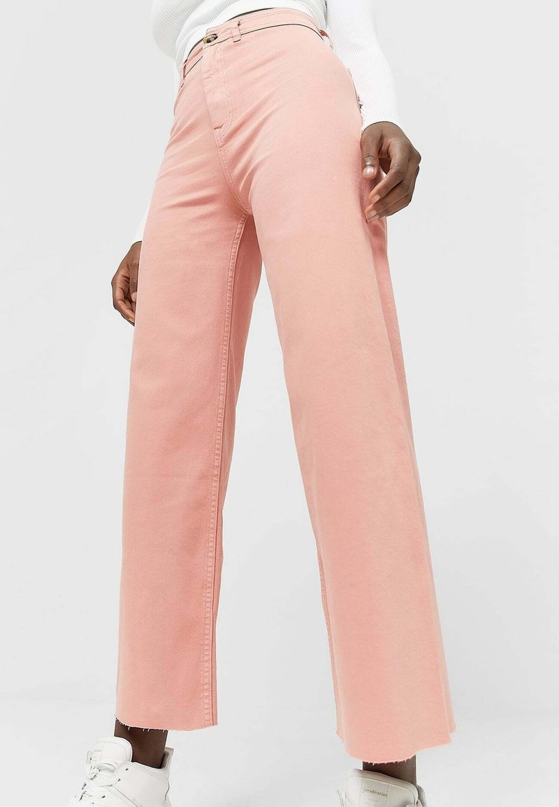 Jeans a gamba larga di colore rosa chiaro, realizzati in cotone. Presentano un vita alta, cuciture a contrasto e una leggera frangia all'orlo.